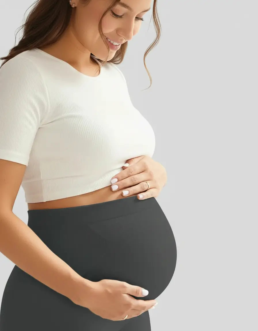 Smiling pregnant woman in a white crop top and dark gray soft-stretch full-length maternity leggings.