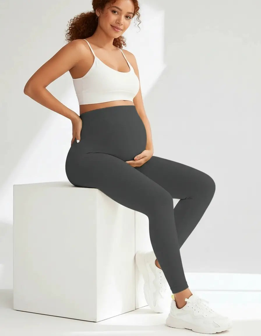 Smiling pregnant woman wearing charcoal grey full-length soft-stretch maternity leggings and a white crop top.