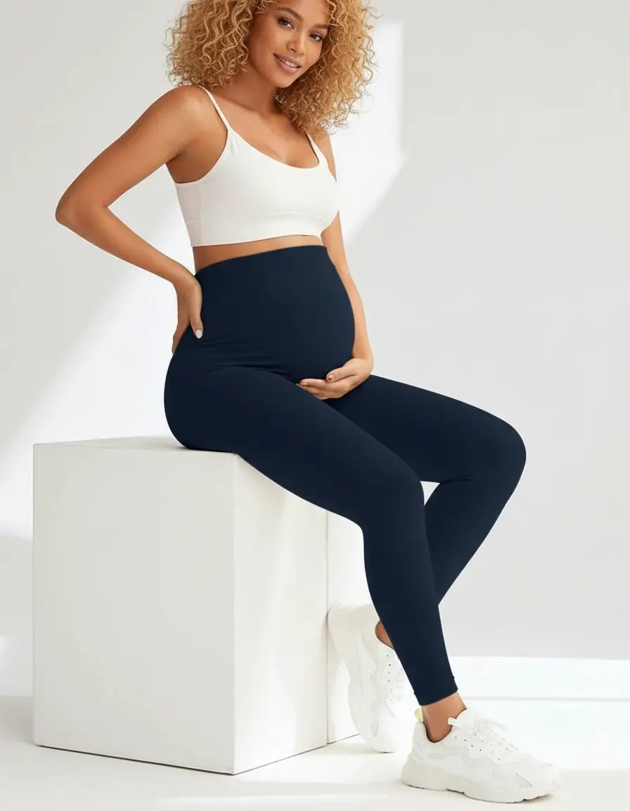 Smiling pregnant woman in navy soft-stretch full-length maternity leggings and a white crop top.
