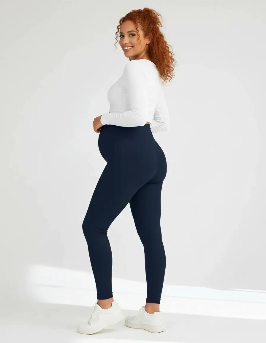 Smiling pregnant woman in navy soft-stretch full-length maternity leggings and a white long-sleeve top.
