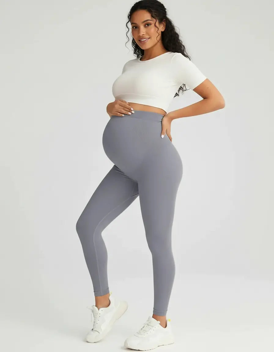 Pregnant woman in soft-stretch, full-length gray maternity leggings and a white crop top.