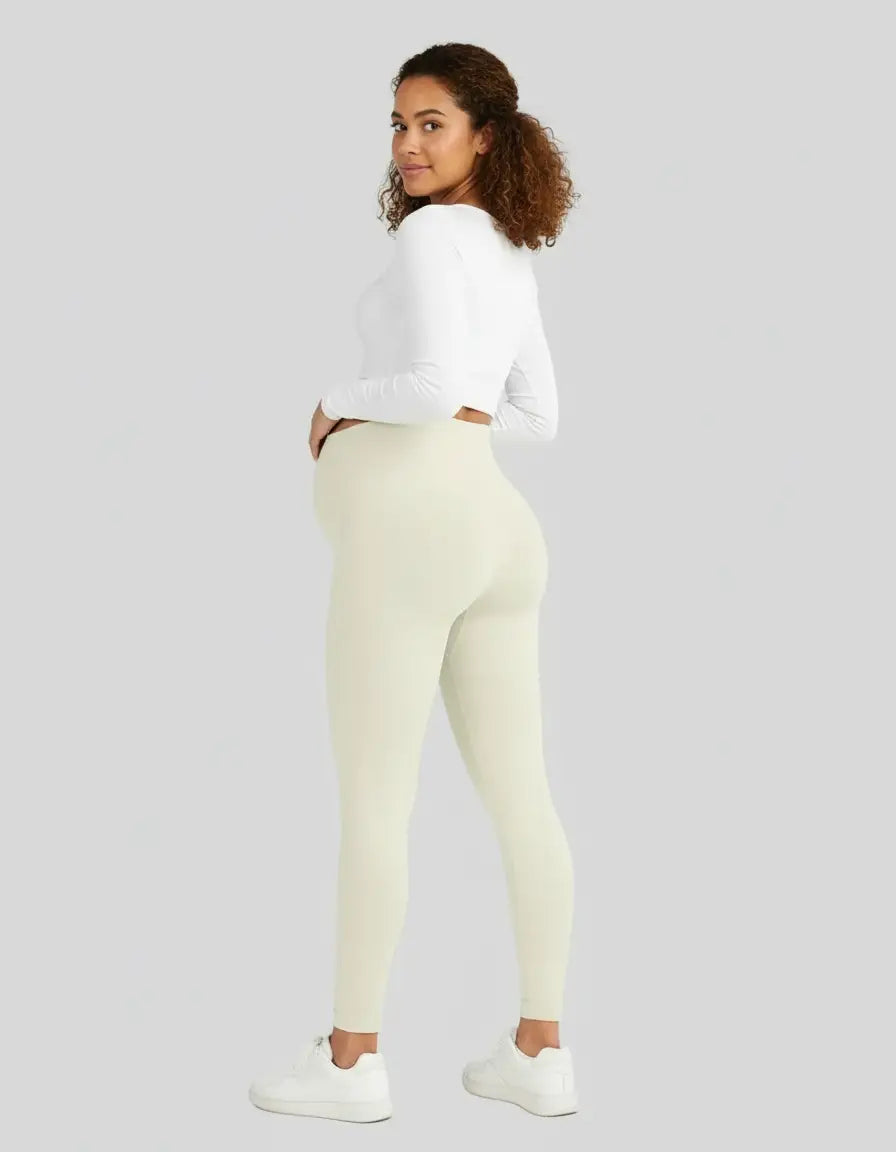 Pregnant woman wearing soft-stretch full-length maternity leggings in a light cream color, paired with a white top.