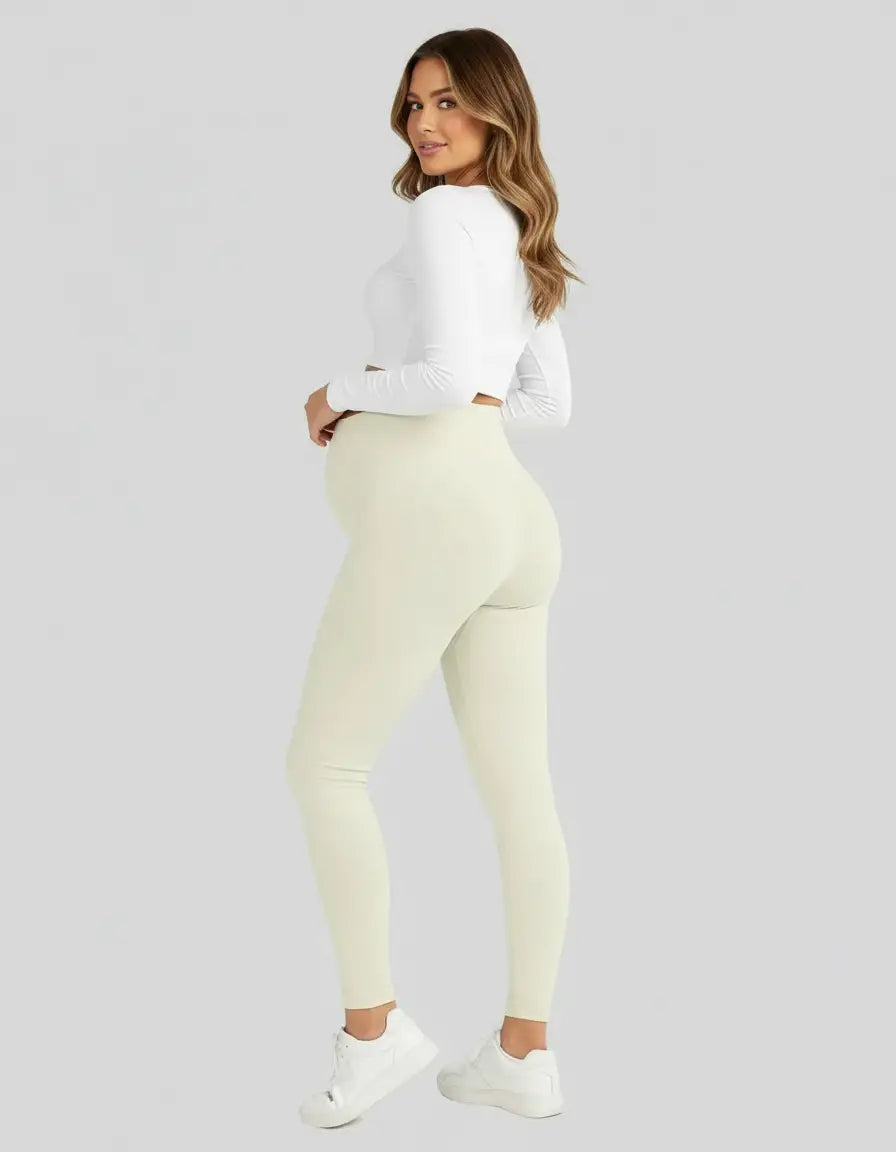 Pregnant woman in soft-stretch, full-length cream maternity leggings and a white long-sleeve top.