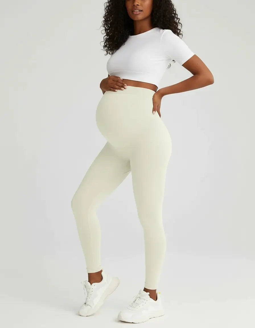 Pregnant woman in soft-stretch, full-length cream maternity leggings and a white crop top.