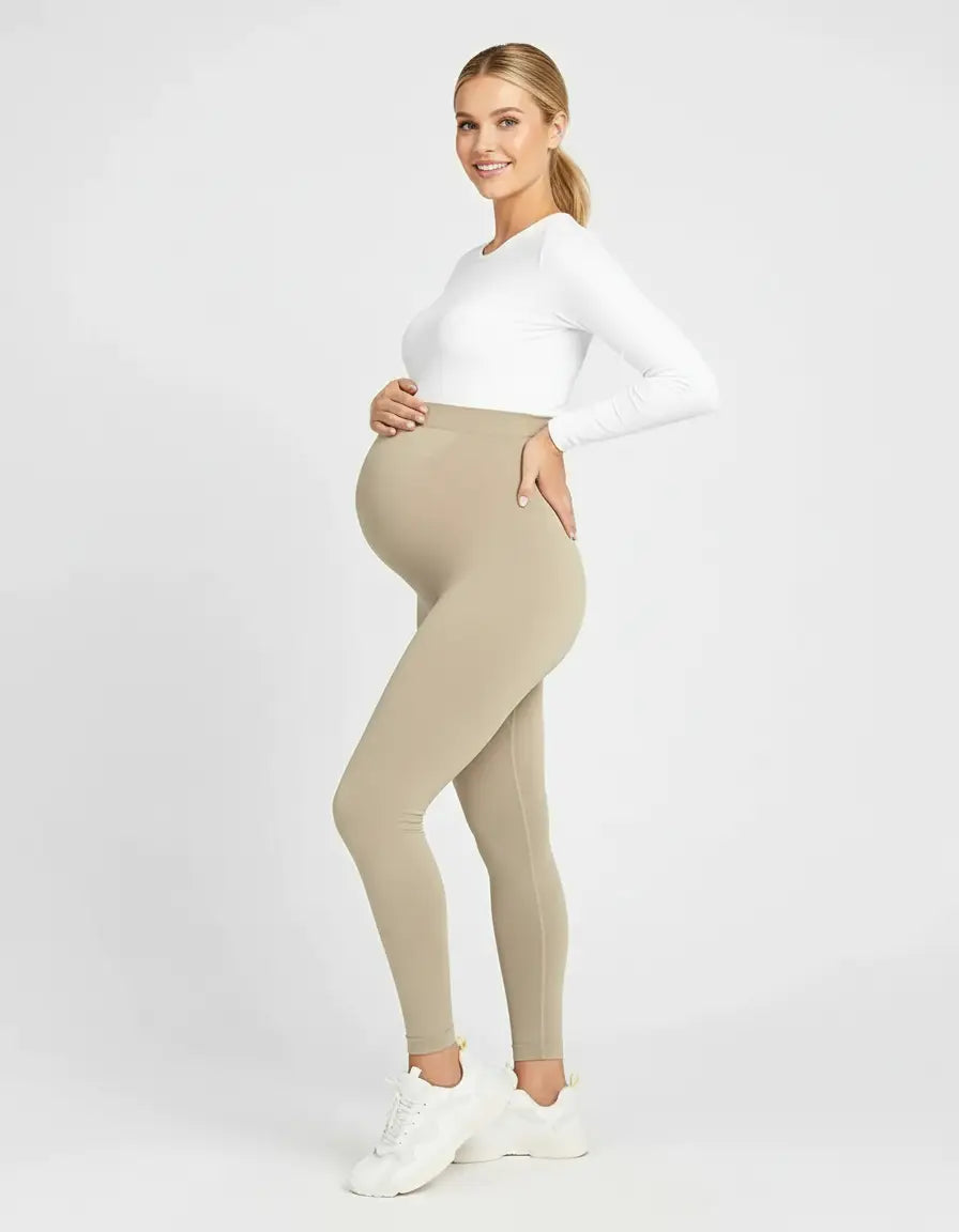 Smiling pregnant woman in full-length, soft-stretch beige maternity leggings and a white long-sleeve top.