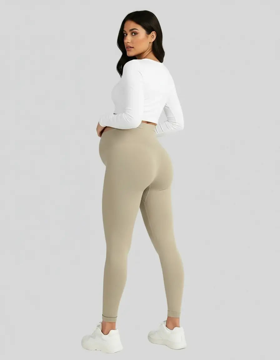 Pregnant woman in soft-stretch, full-length beige maternity leggings and a white long-sleeve top.