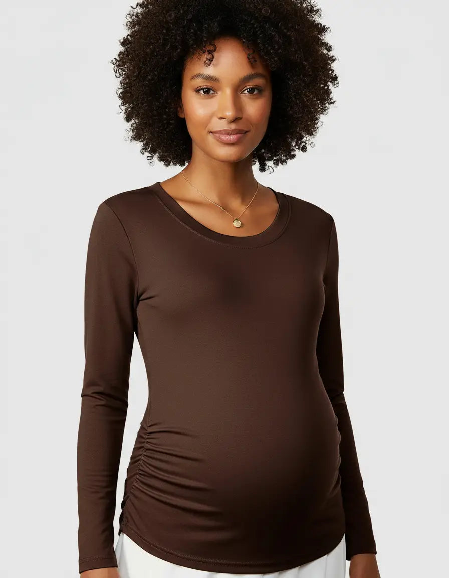 Woman in a brown long-sleeve maternity top with side ruching, a gold necklace, and curly hair.