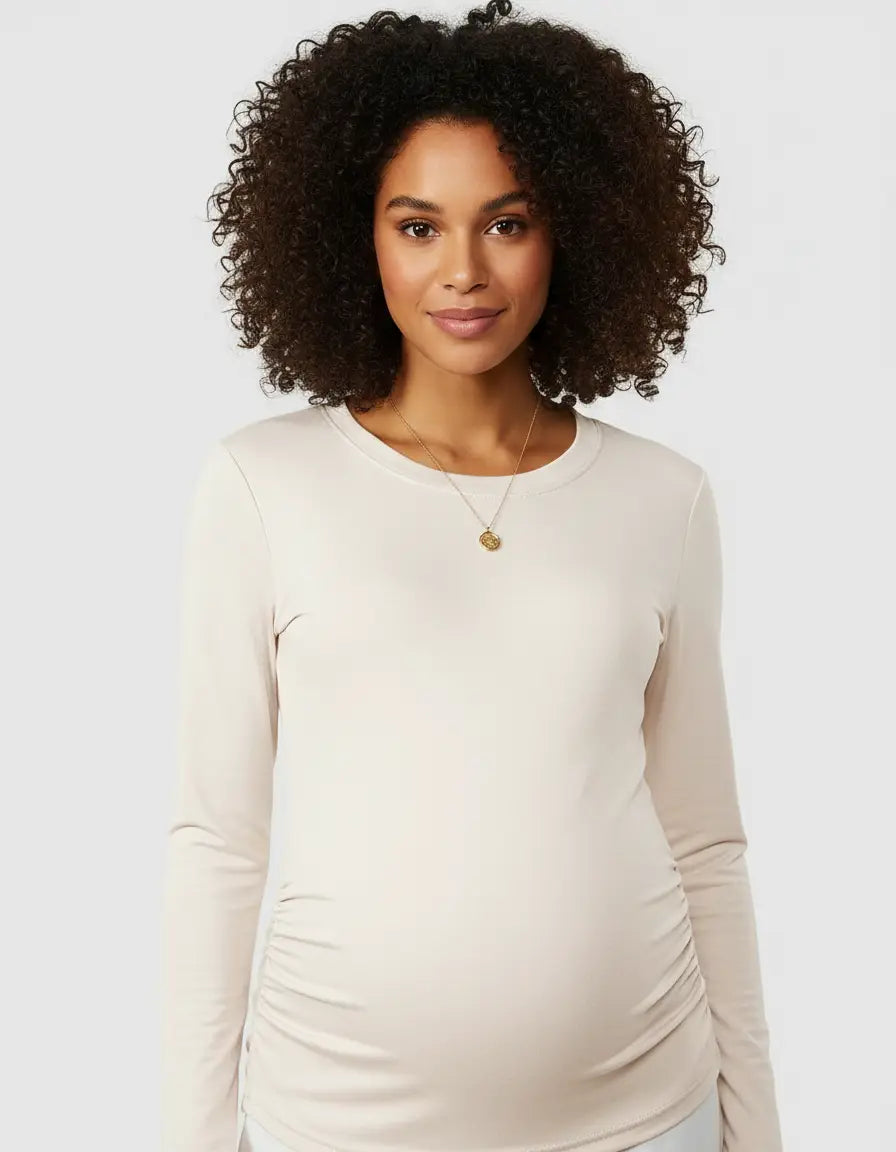 Smiling pregnant woman in a cream long-sleeve thermal maternity top with side ruching.