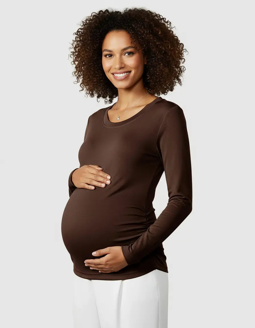 Smiling pregnant woman in a brown long-sleeve thermal maternity top with ruched sides, holding her belly.