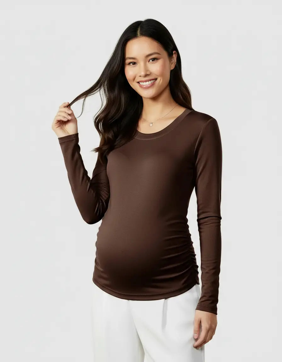 Smiling pregnant woman models a brown thermal long sleeve maternity top with side ruching and white pants.