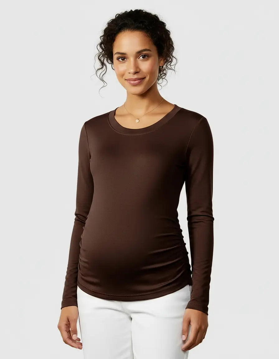 Smiling pregnant woman wearing a brown long-sleeve thermal maternity top with side ruching and white pants.
