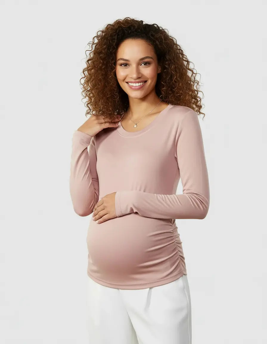 Smiling pregnant woman in a soft pink thermal long-sleeve maternity top with side ruching and white pants.