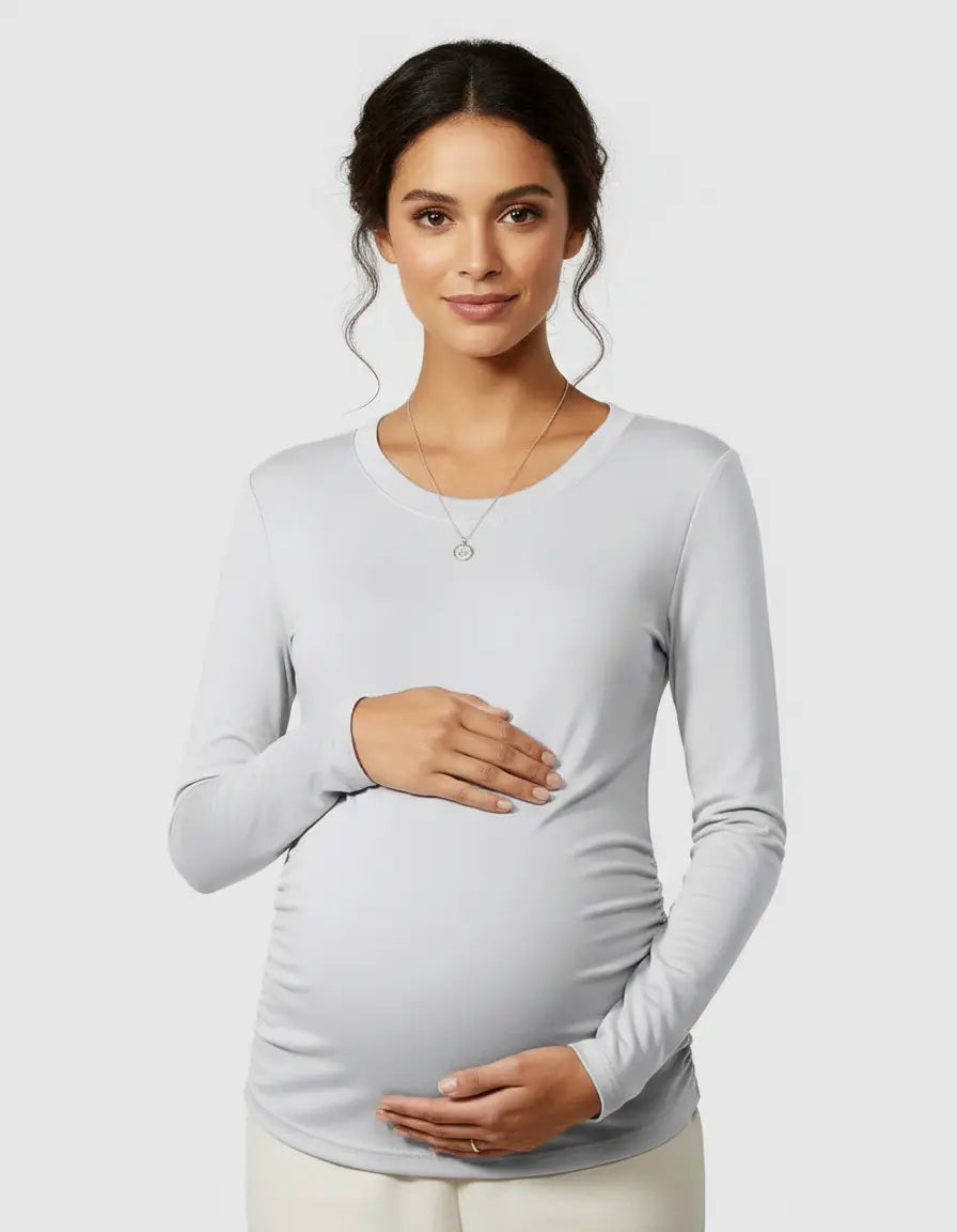 Pregnant woman in a light grey long-sleeve thermal maternity top, gently holding her baby bump.