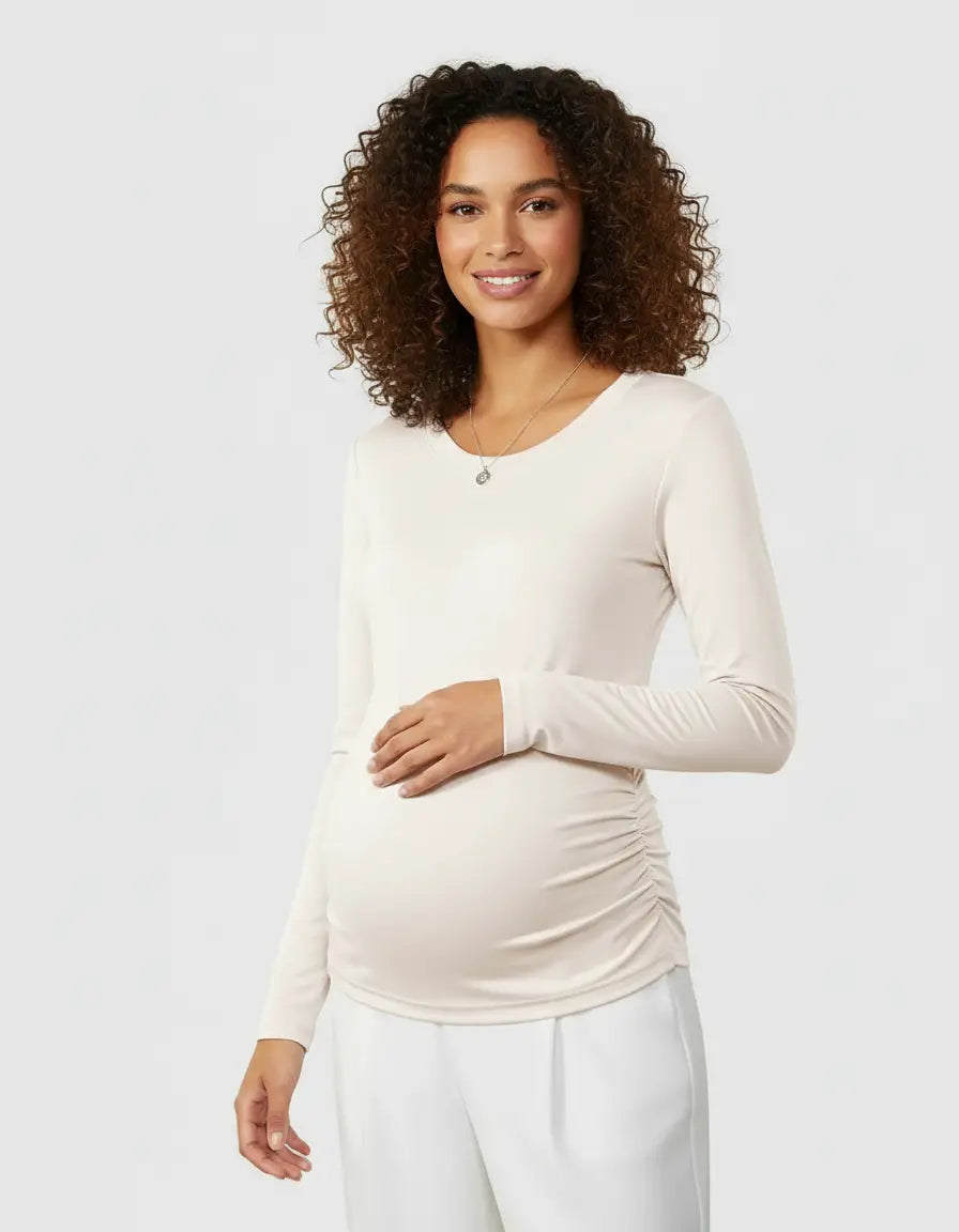 Smiling pregnant woman in a cream long-sleeve thermal maternity top with side ruching and white pants.