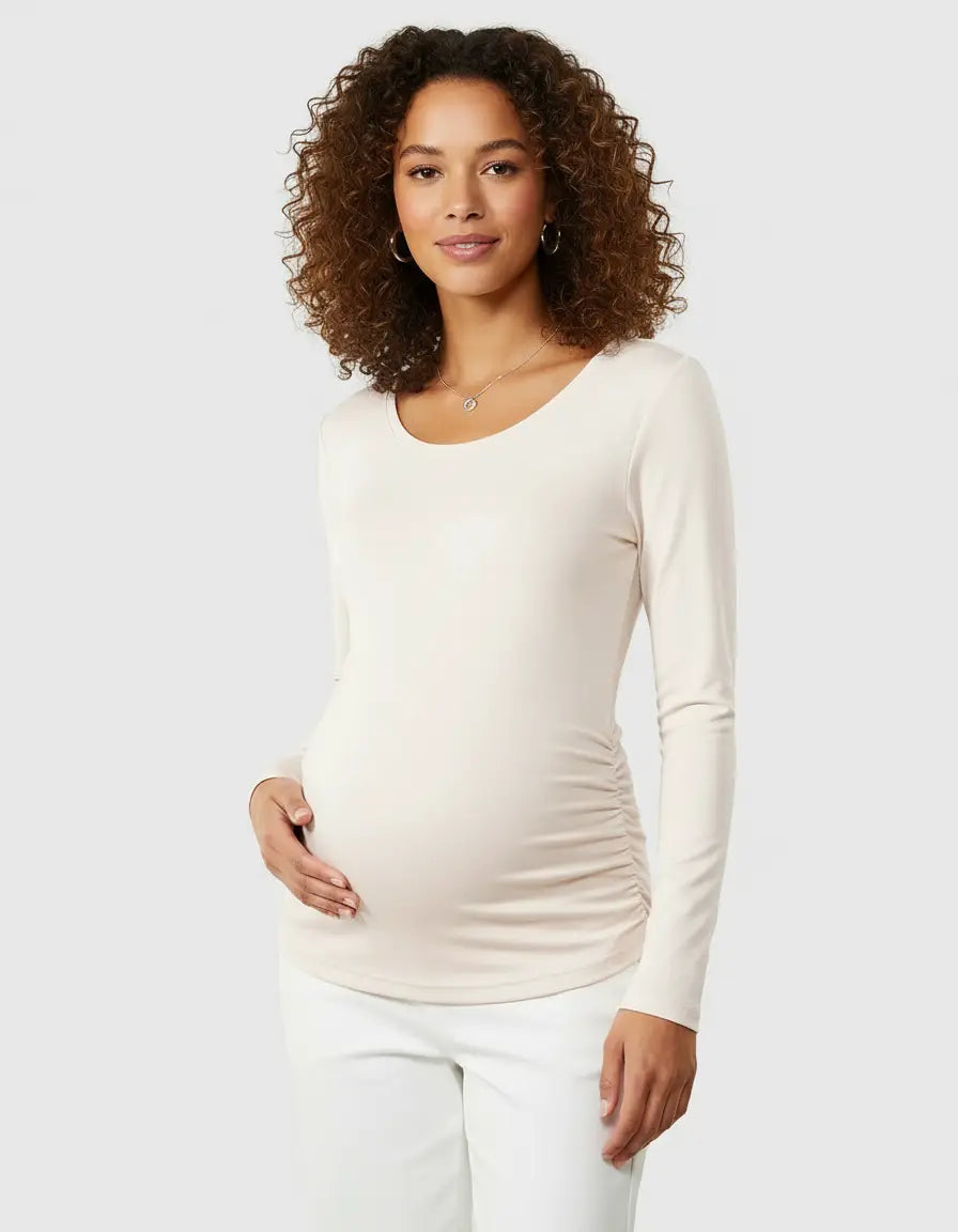 Woman in a cream long-sleeve thermal maternity top with side ruching, designed for comfort.
