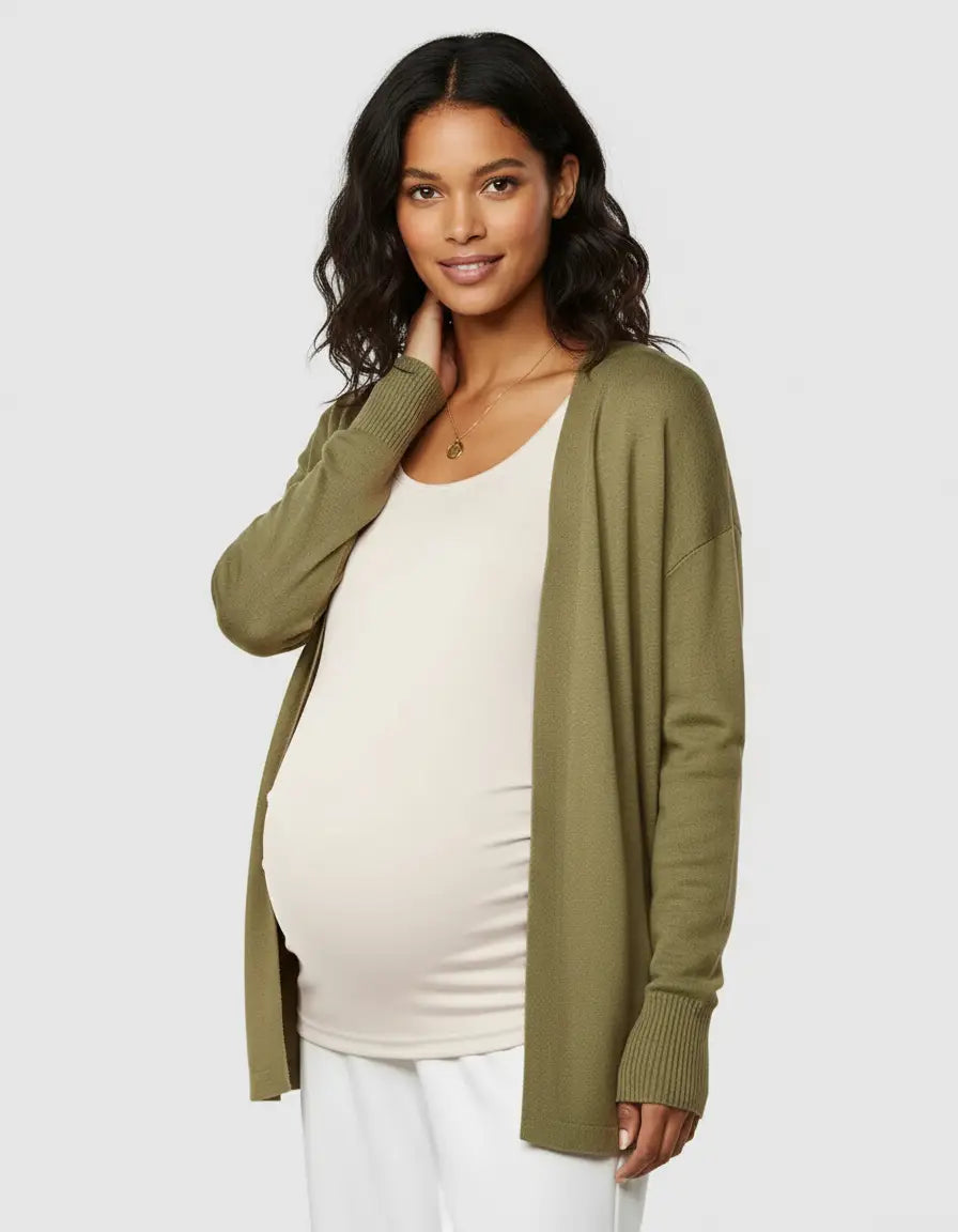 Pregnant woman in a cream thermal maternity top, olive green cardigan, and white pants.