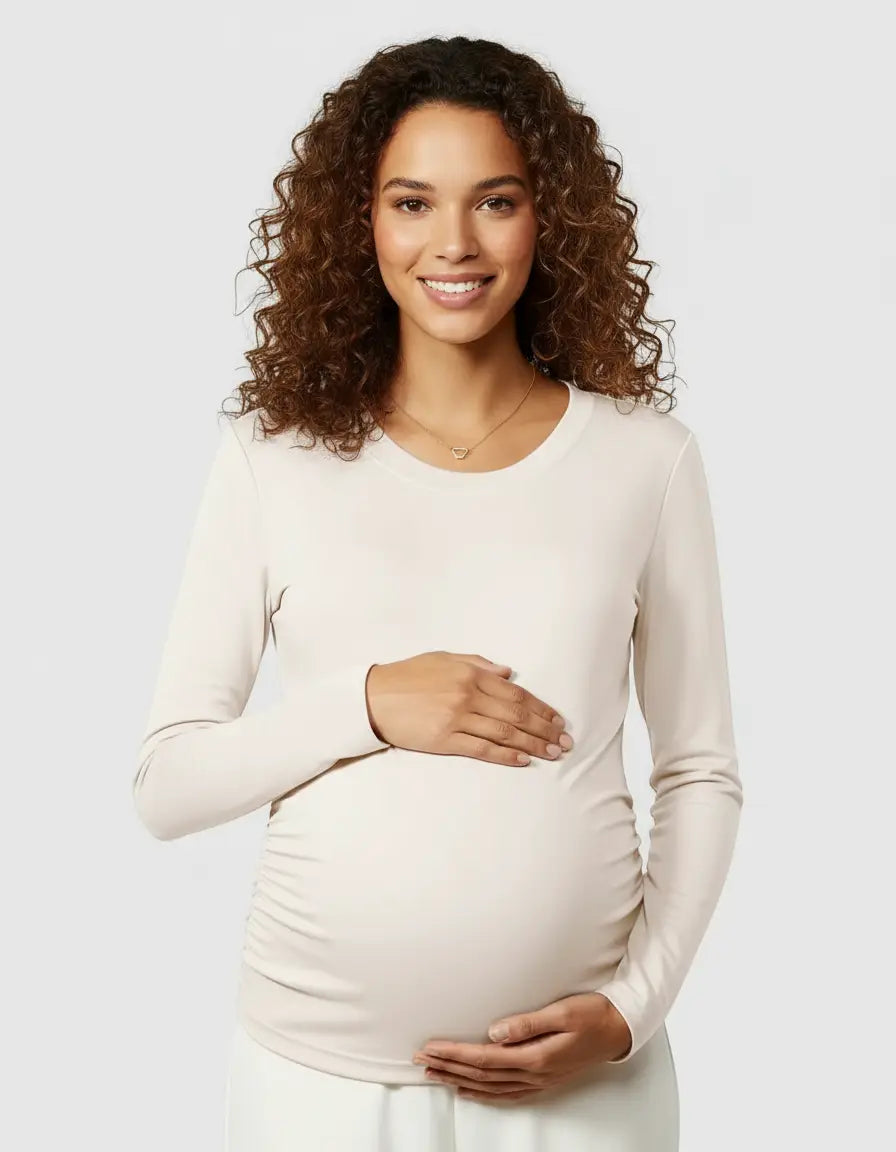 Smiling pregnant woman in a cream long-sleeve thermal maternity top with ruched sides.