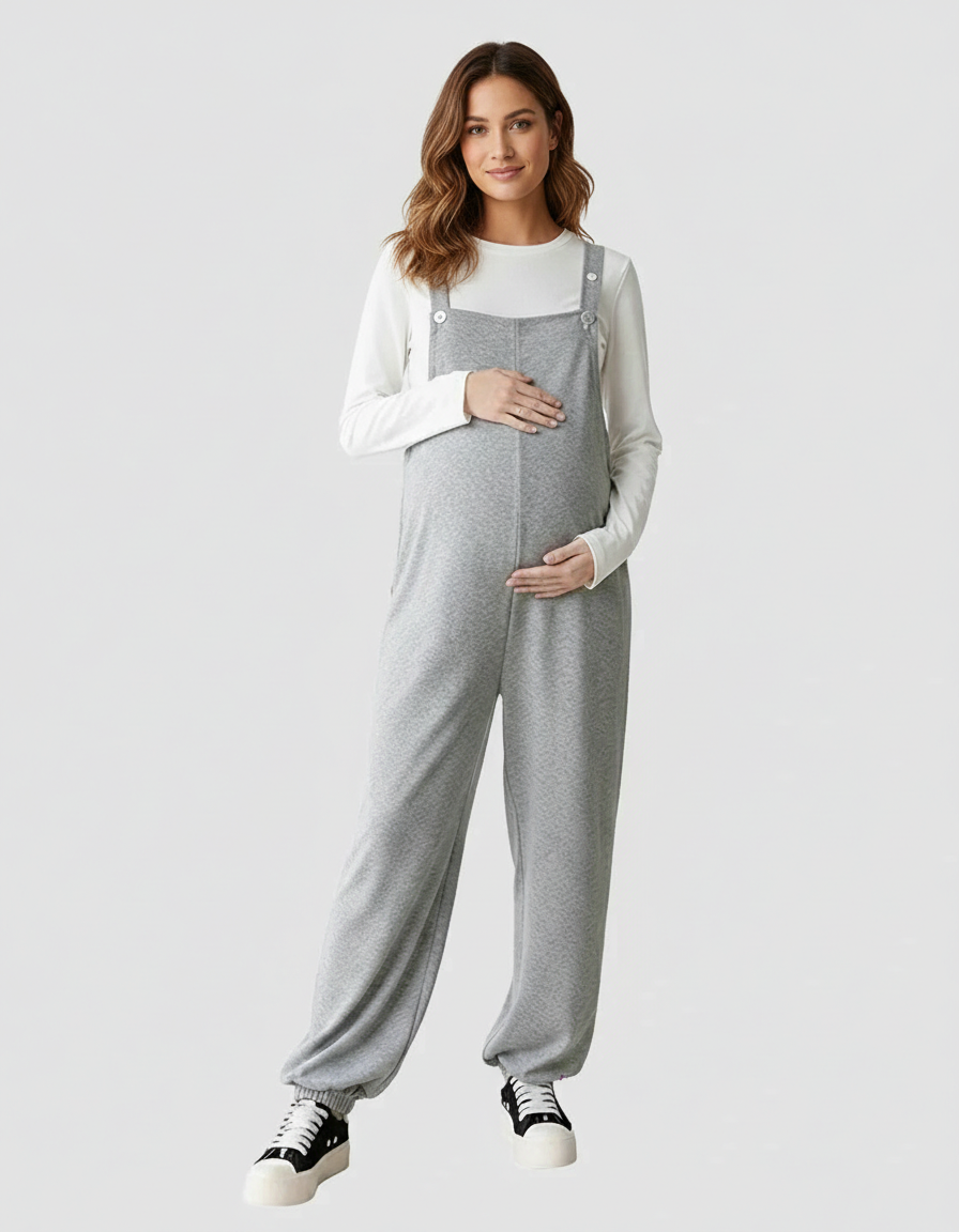 Pregnant woman in grey wide-leg maternity overalls with suspended straps and a white long-sleeve top.