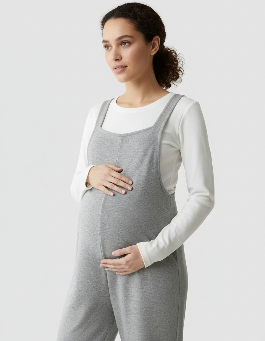 Pregnant woman in gray suspended-strap wide-leg maternity overalls over a white long-sleeve top.