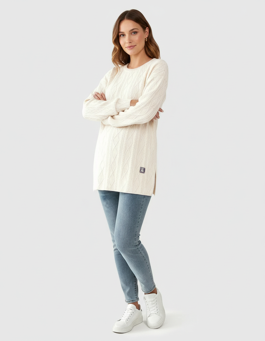 Woman in a cream textured loose-fit maternity top with cable knit pattern, paired with jeans and white sneakers.