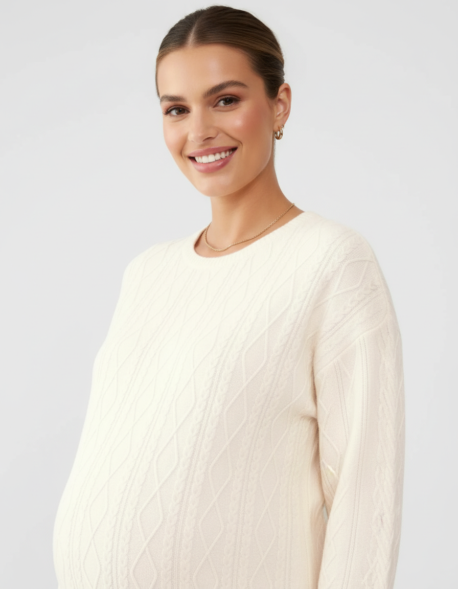 Smiling pregnant woman in a cream textured loose-fit maternity top with cable knit details.