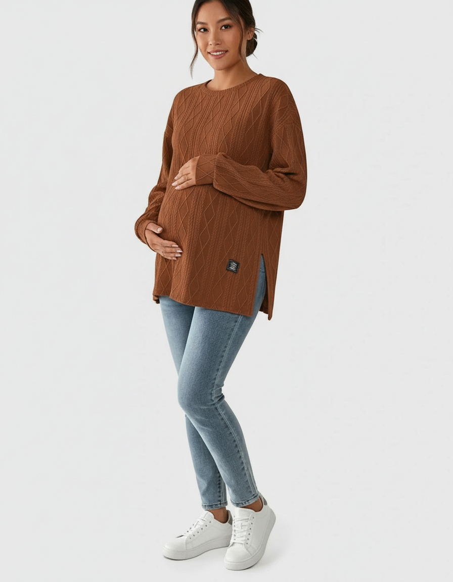 Pregnant woman in a brown textured loose-fit maternity top with side slits, light wash jeans, and white sneakers.