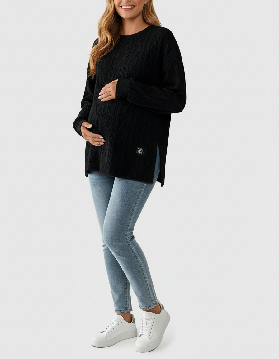 Pregnant woman in a black textured loose-fit maternity top with side slits, light blue jeans, and white sneakers.