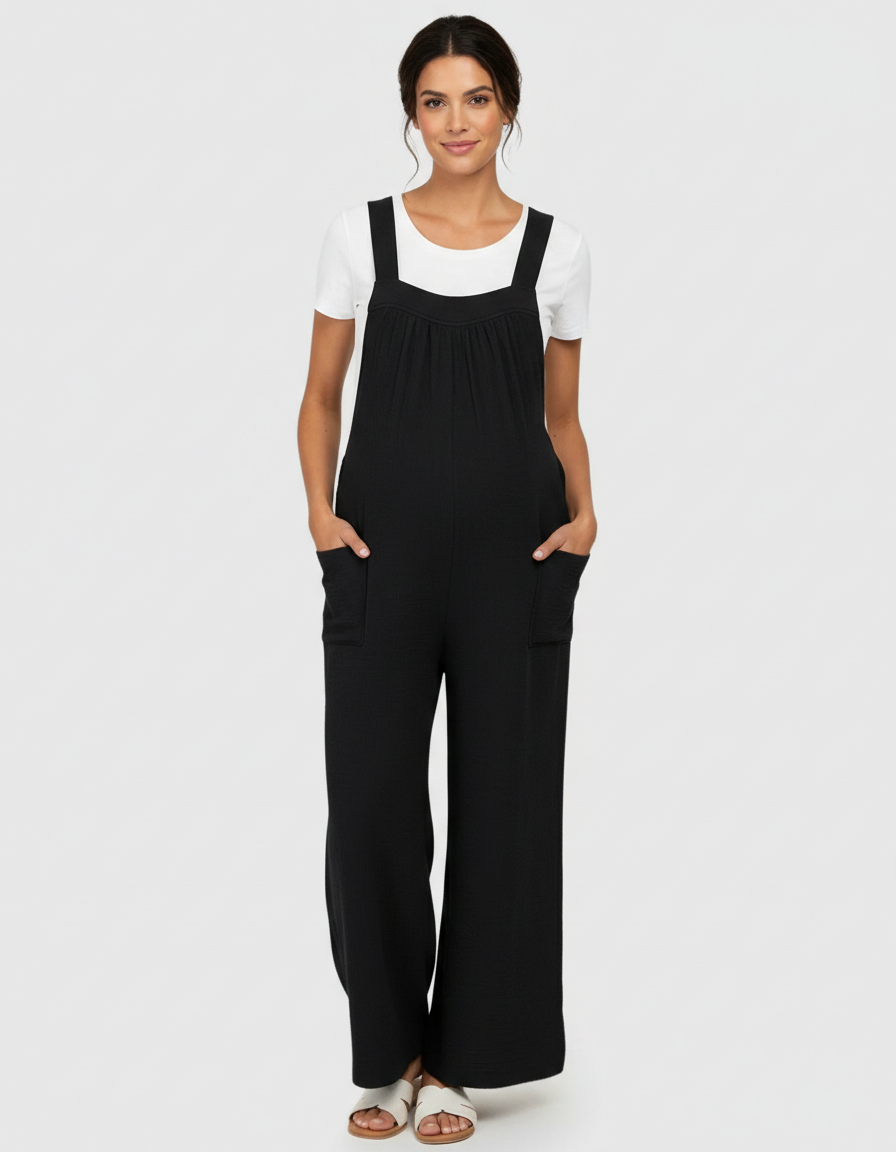 Woman wearing a black tie-back wide-leg maternity jumpsuit over a white tee, with pockets.