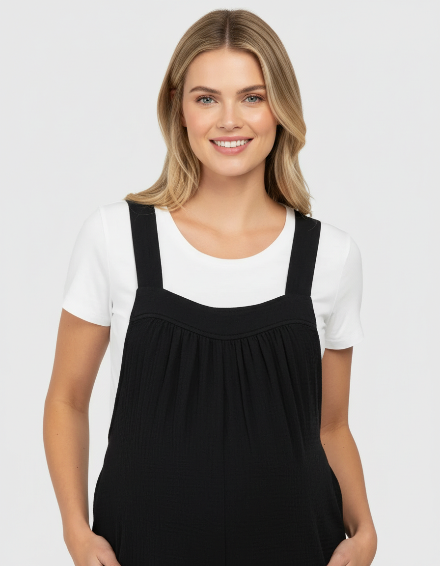 Smiling pregnant woman in a black tie-back wide-leg maternity jumpsuit over a white tee.