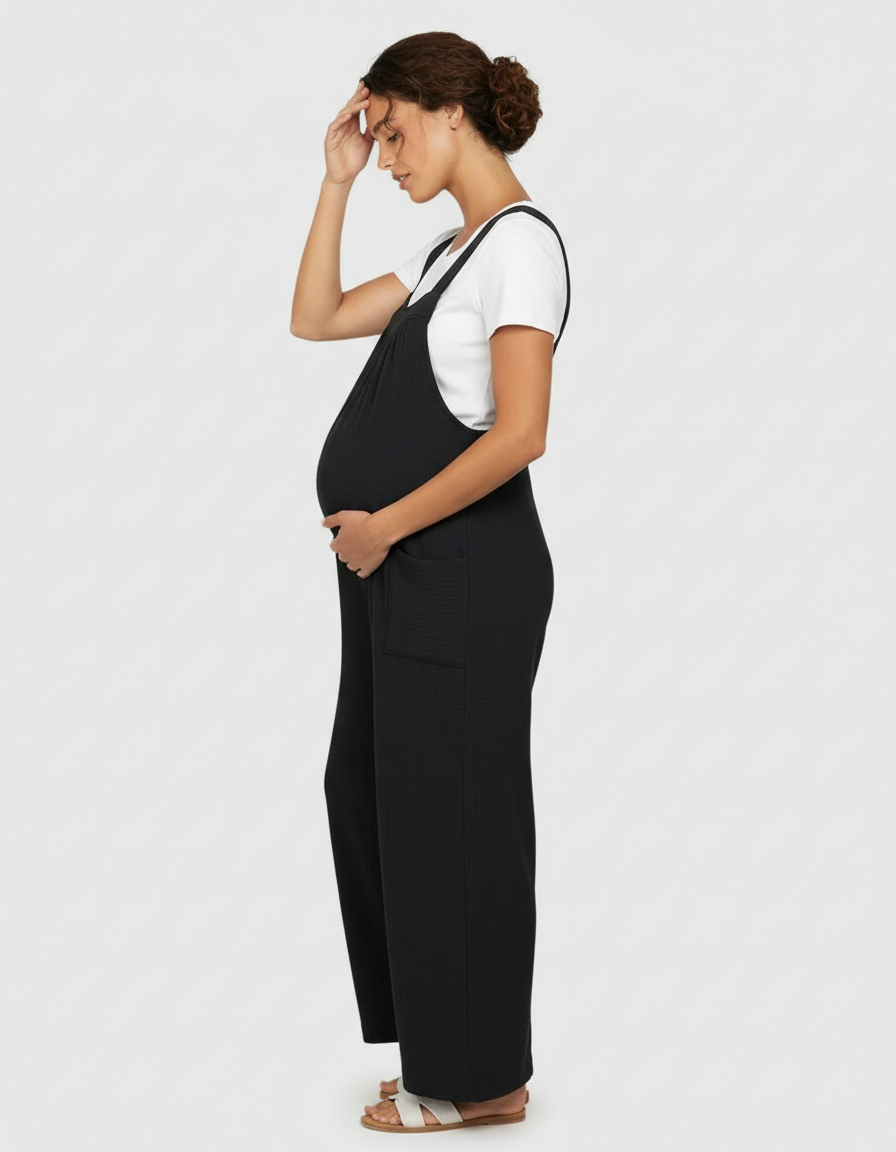 Pregnant woman in black ribbed wide-leg maternity jumpsuit with white tee and tie-back detail.