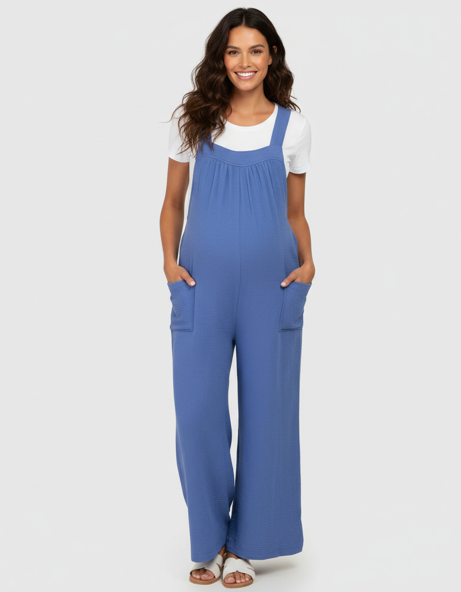Smiling pregnant woman in a blue wide-leg maternity jumpsuit with pockets and a white tee.