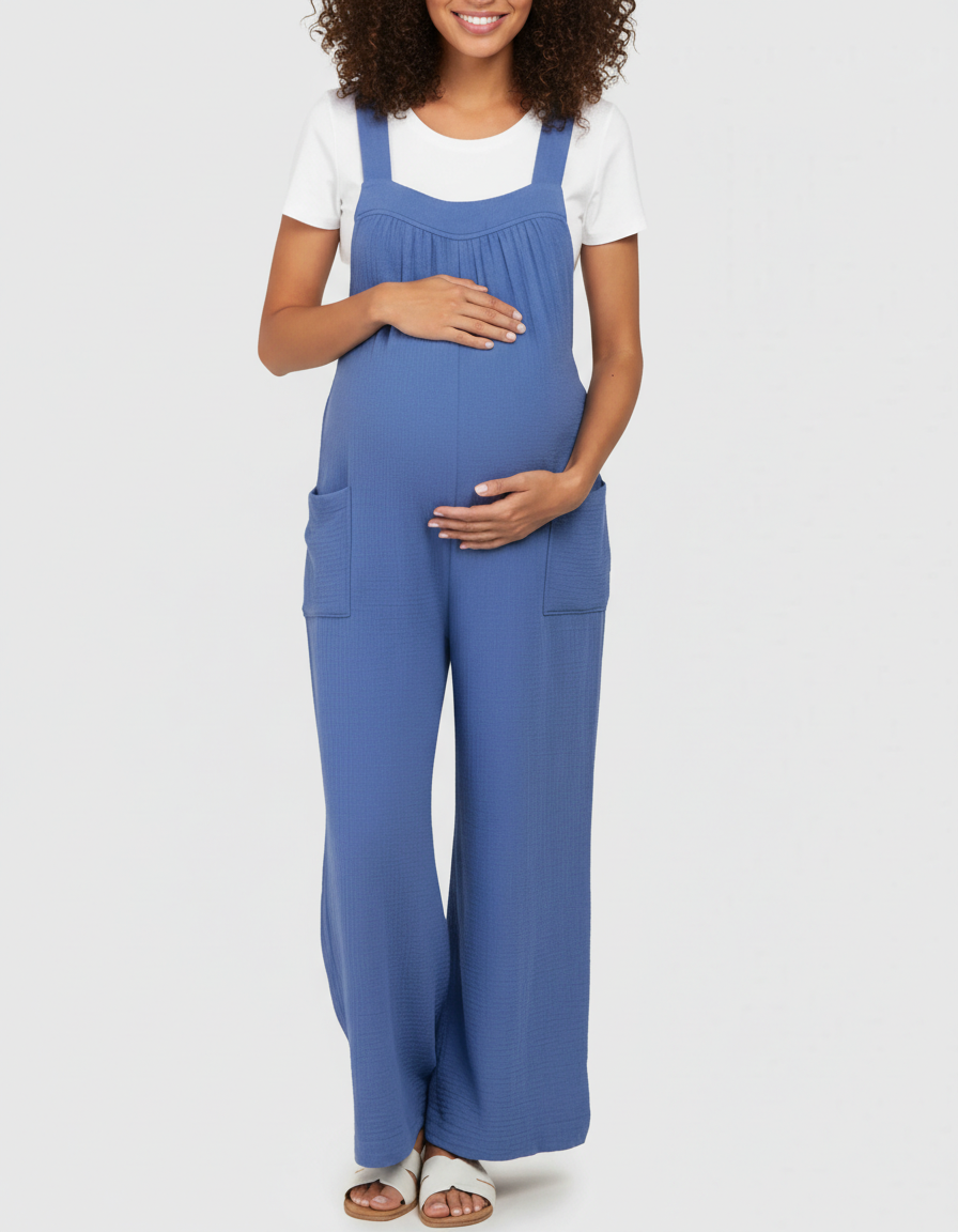 Smiling pregnant woman in a blue wide-leg maternity jumpsuit with pockets and a white tee.