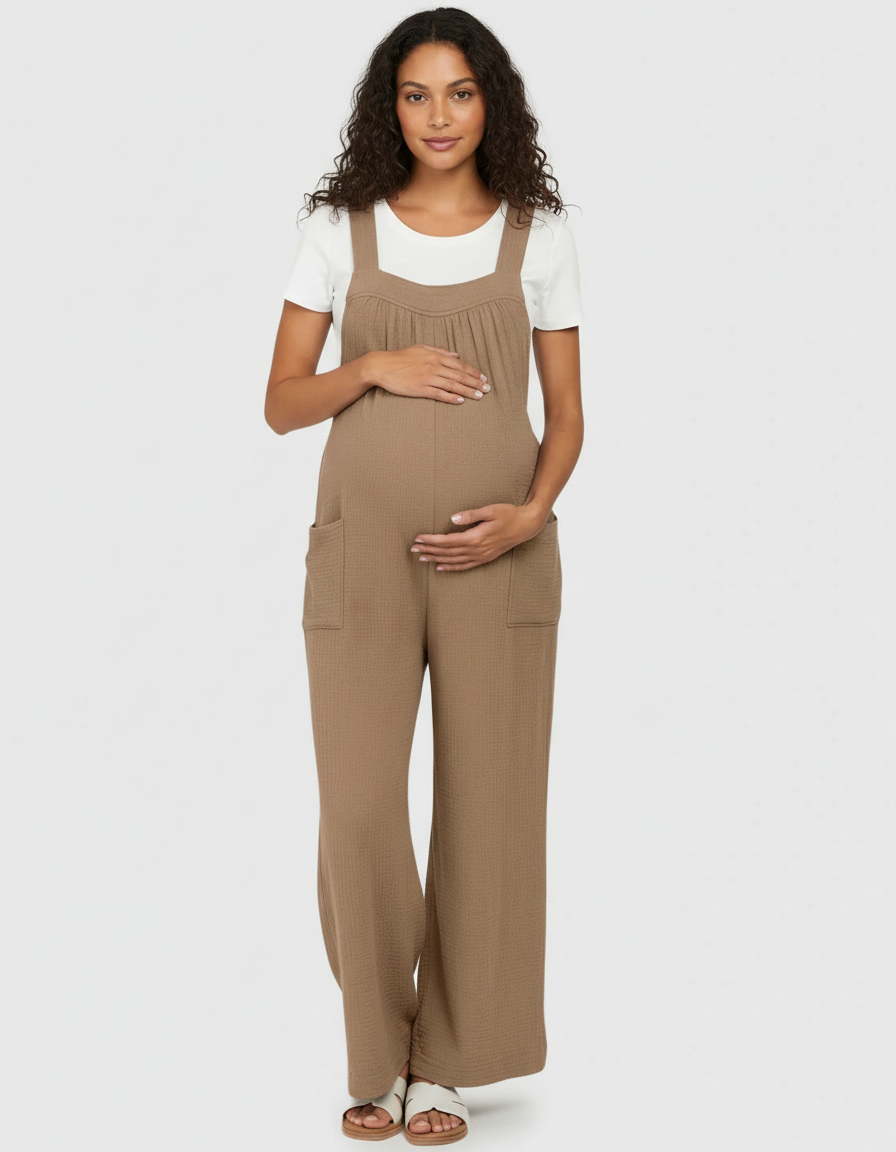 Pregnant woman in a brown textured wide-leg maternity jumpsuit with front pockets and a white tee.