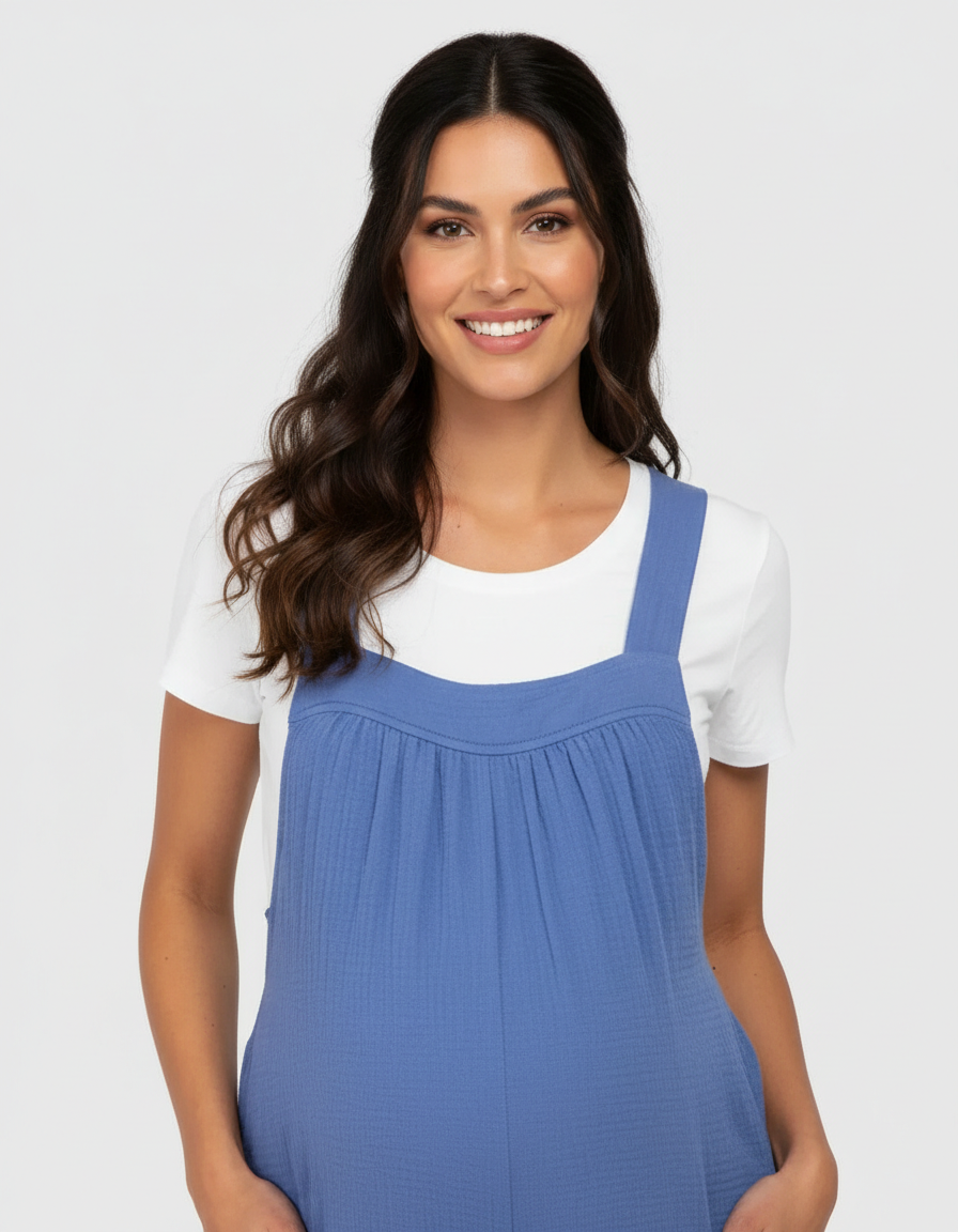 Smiling pregnant woman in a blue tie-back wide-leg maternity jumpsuit over a white t-shirt.
