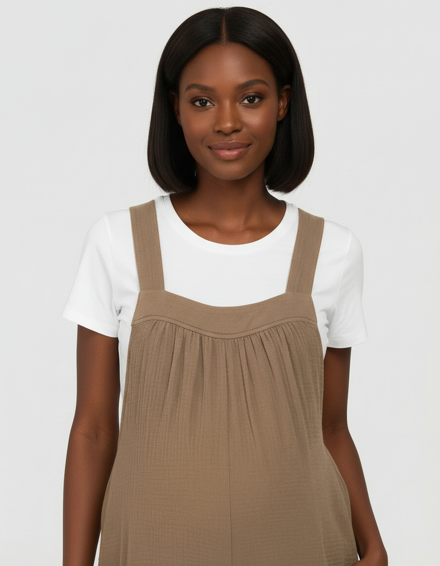 Smiling woman in a brown tie-back wide-leg maternity jumpsuit over a white tee.