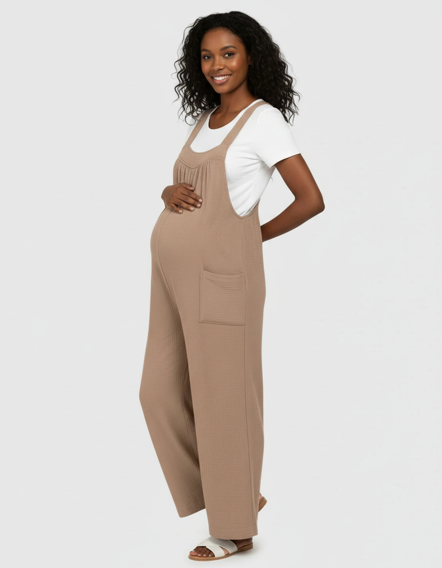 Smiling pregnant woman in a beige waffle knit wide-leg maternity jumpsuit with a white tee.