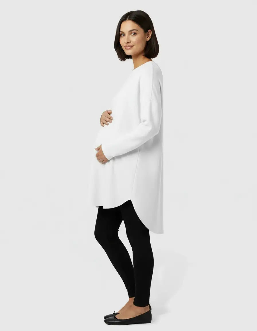Pregnant woman in a white relaxed-fit wool blend maternity sweater and black leggings.