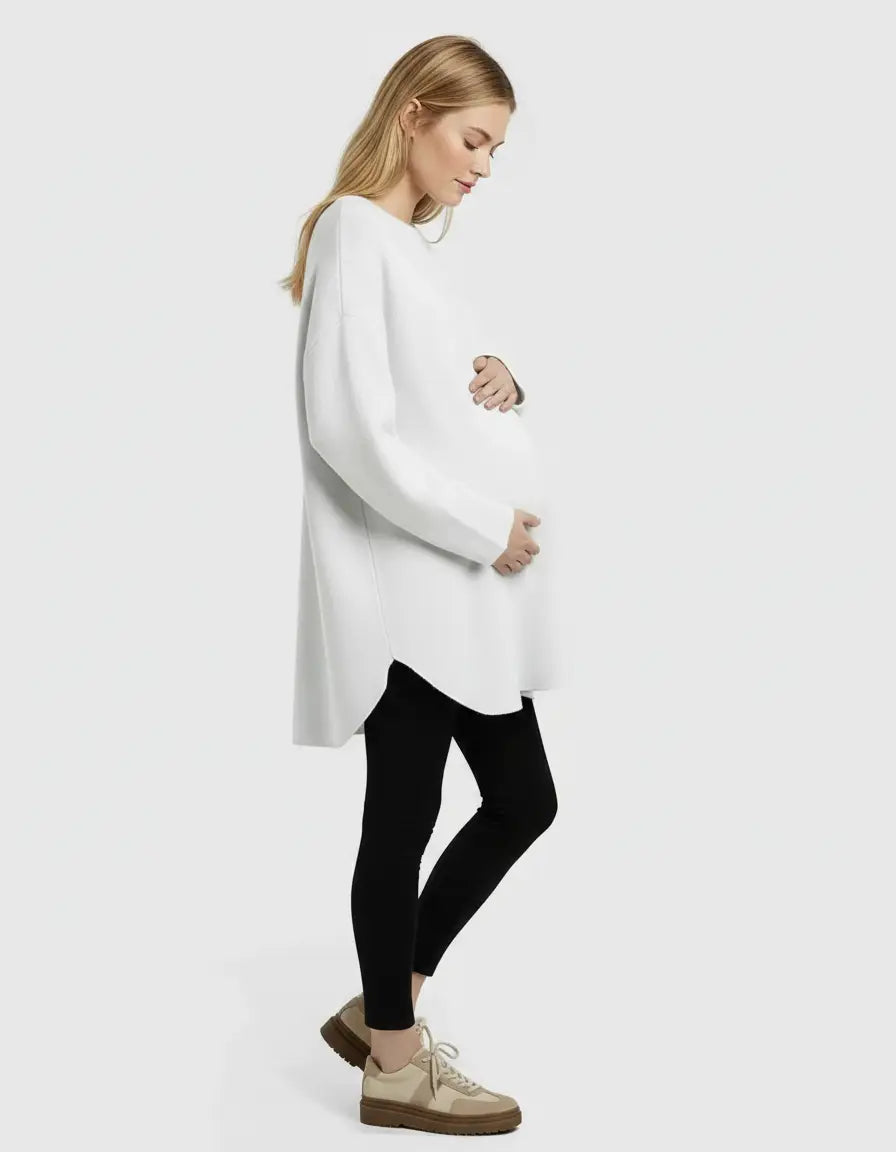 Blonde pregnant woman wearing a white relaxed-fit wool blend maternity sweater with black leggings.