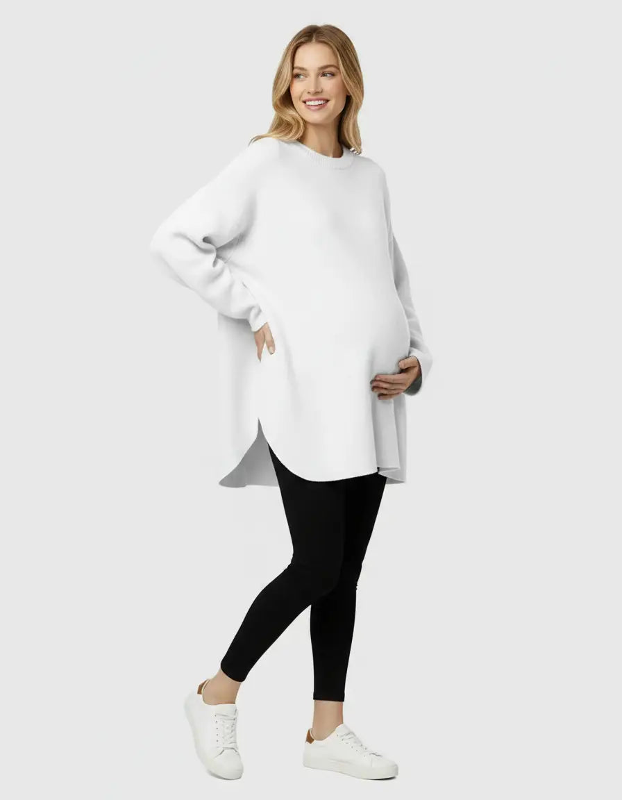 Smiling pregnant woman in a white wool blend relaxed maternity sweater and black leggings.