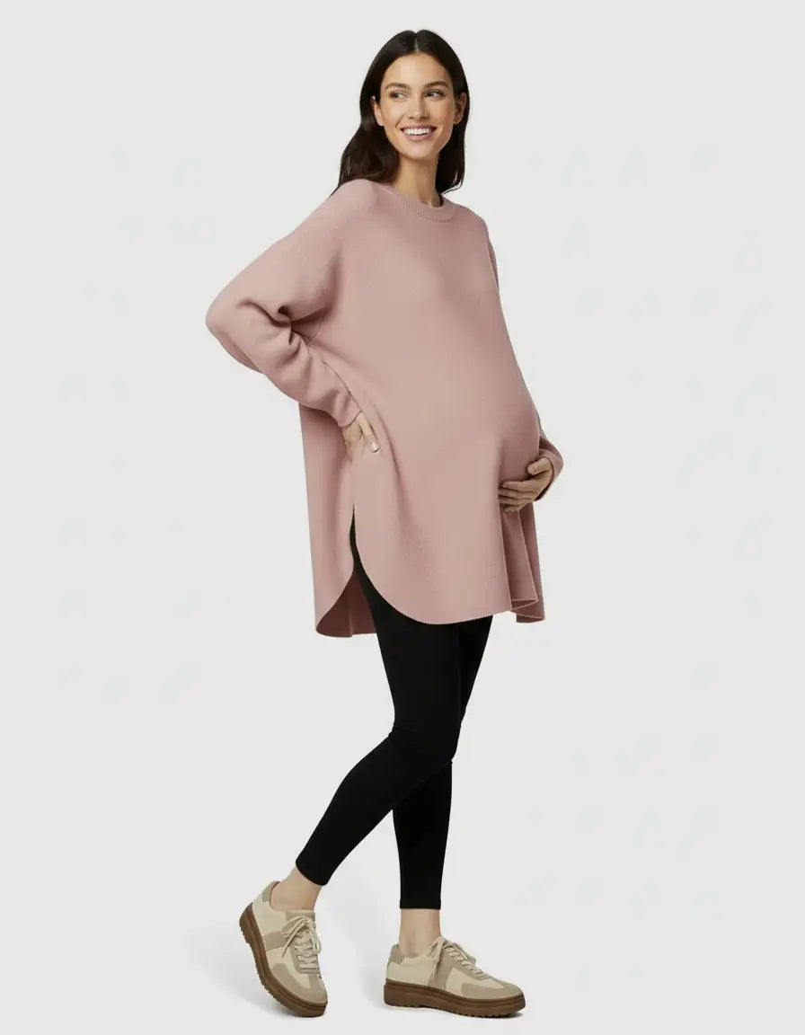 Smiling pregnant woman in a relaxed fit pink wool blend maternity sweater and black leggings.