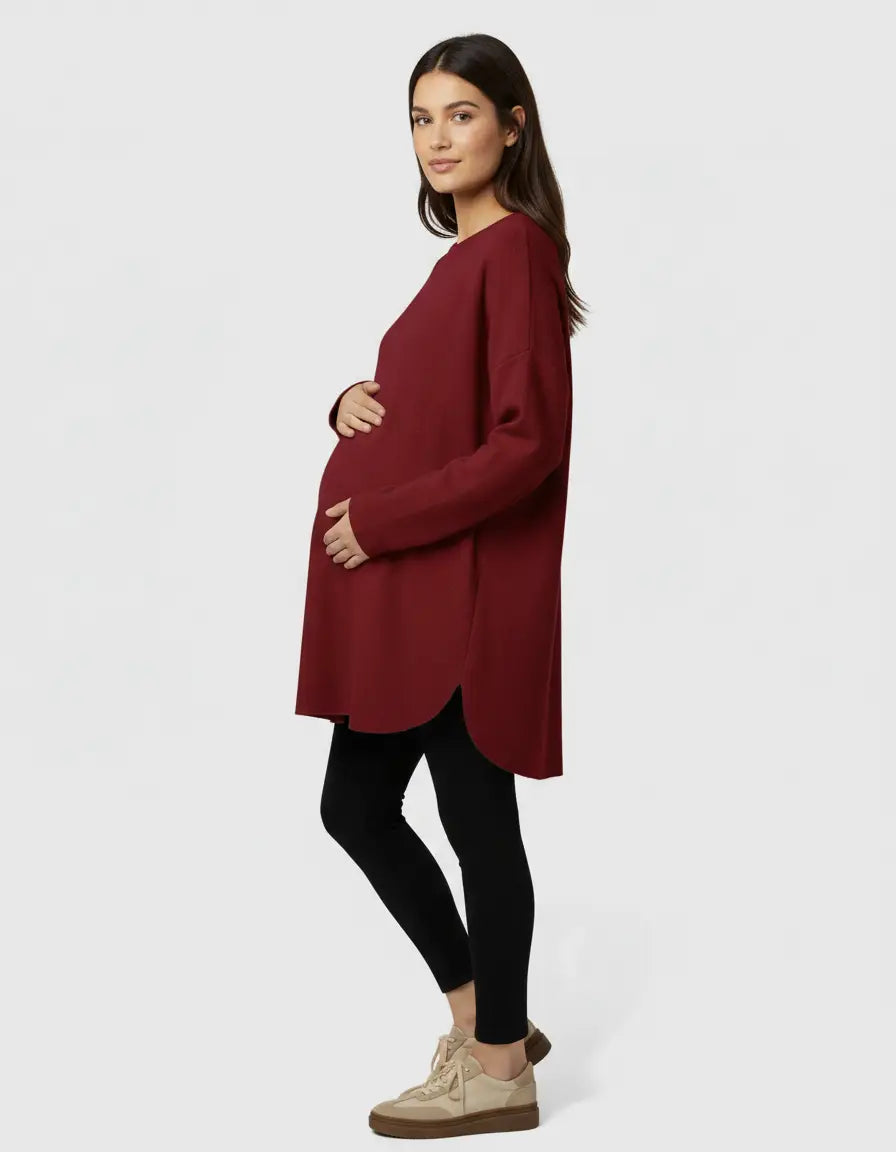 Pregnant woman in a relaxed fit, long-sleeve, dark red wool blend maternity sweater with a curved hem.