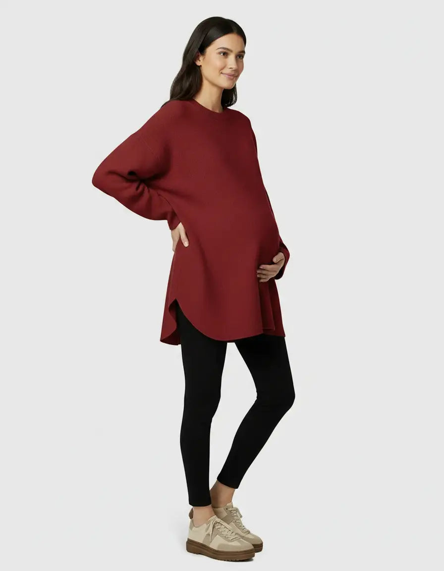 Smiling pregnant woman in a relaxed fit red wool blend maternity sweater and black leggings.