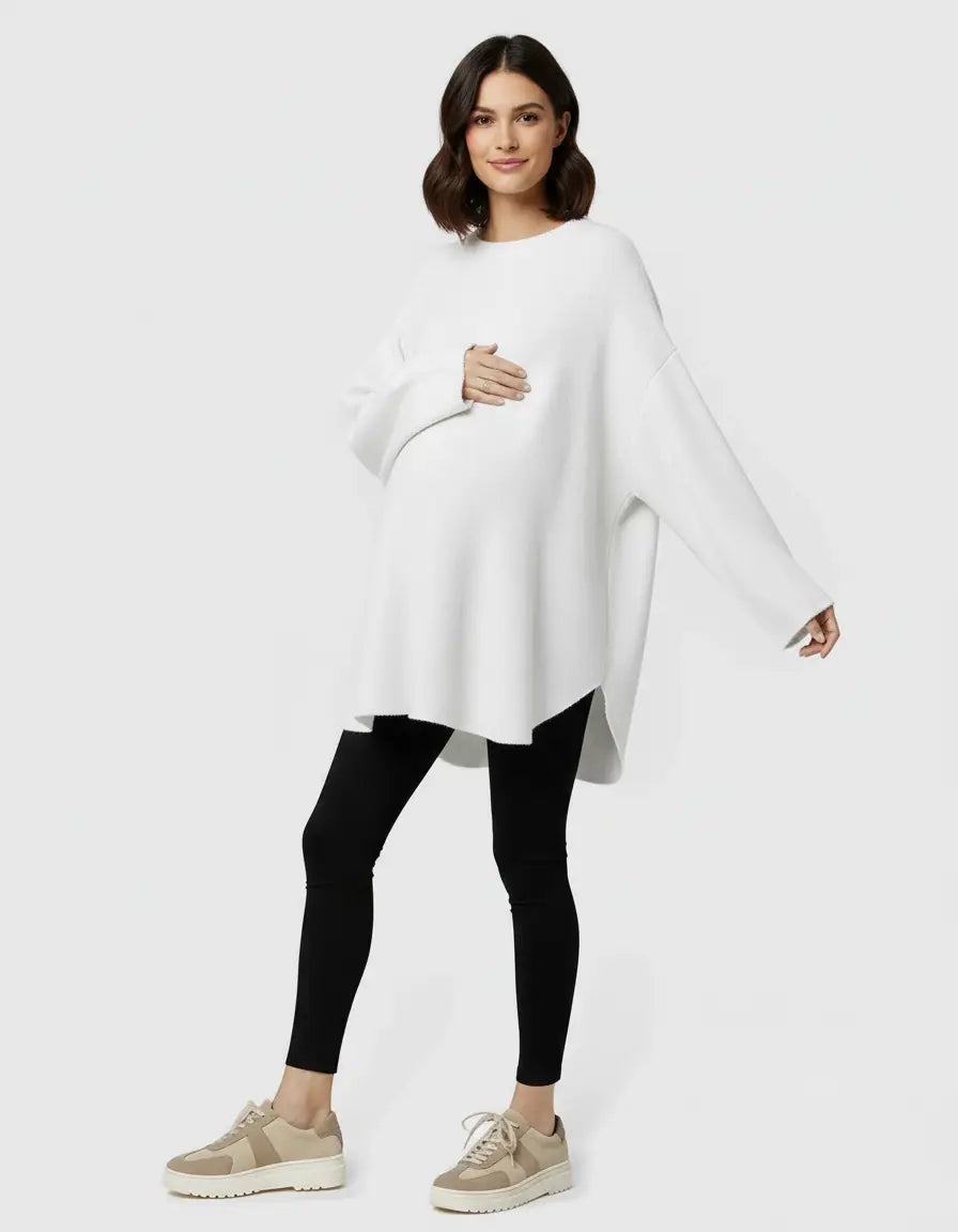 Smiling pregnant woman in a white wool blend relaxed maternity sweater and black leggings.