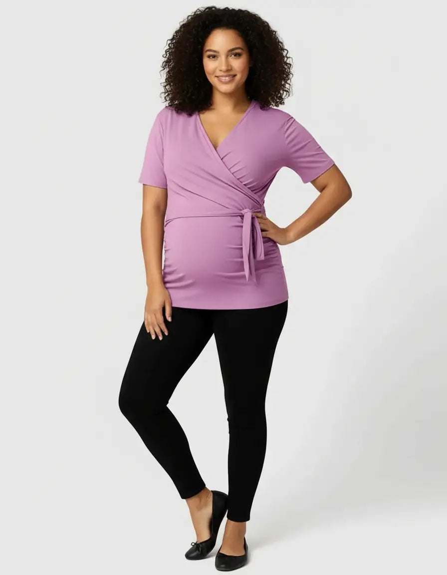 Smiling pregnant woman in a lavender 3-in-1 skin-to-skin nursing wrap top and black leggings.