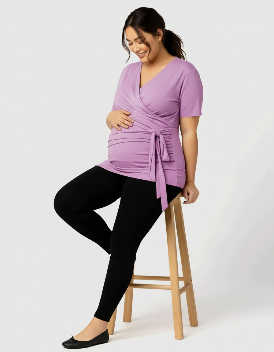 Smiling pregnant woman in a lavender 3-in-1 skin-to-skin nursing wrap top and black leggings.