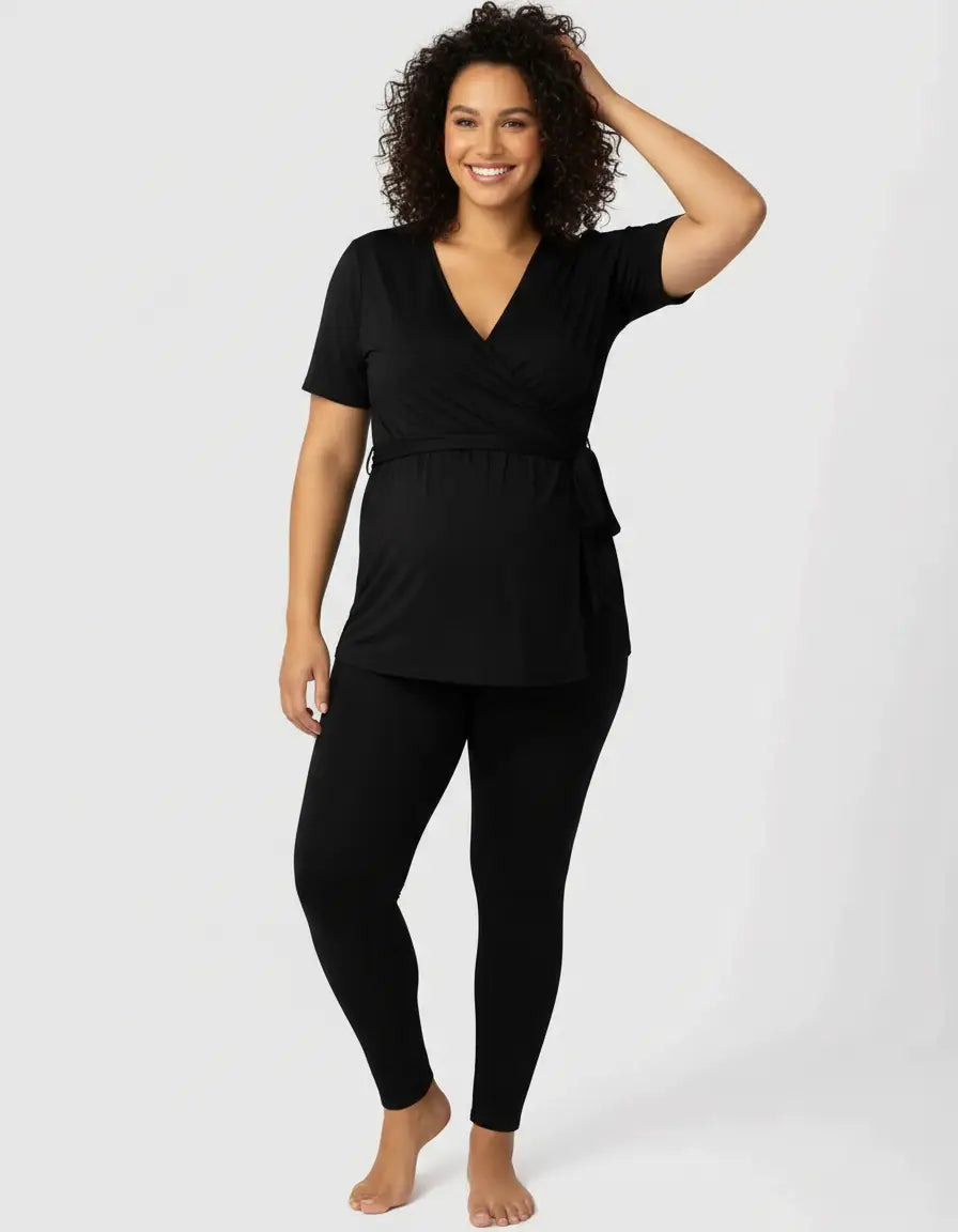Smiling pregnant woman in black 3-in-1 skin-to-skin nursing wrap top and leggings.