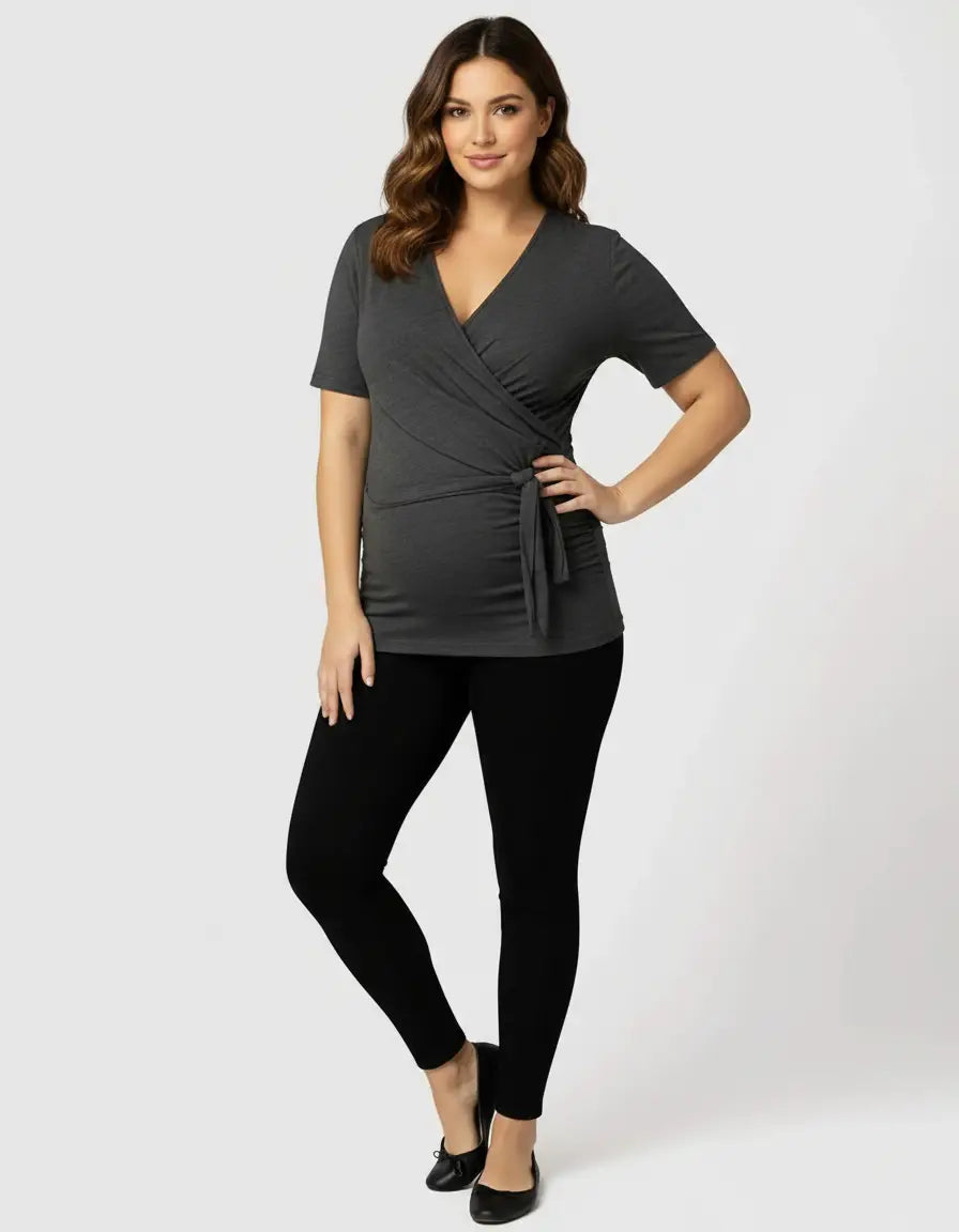 Woman in a charcoal gray 3-in-1 skin-to-skin nursing wrap top with a tie waist and black leggings.