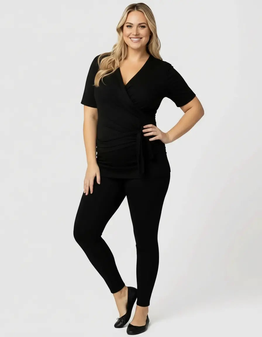 Smiling woman in a black 3-in-1 skin-to-skin nursing wrap top and leggings.