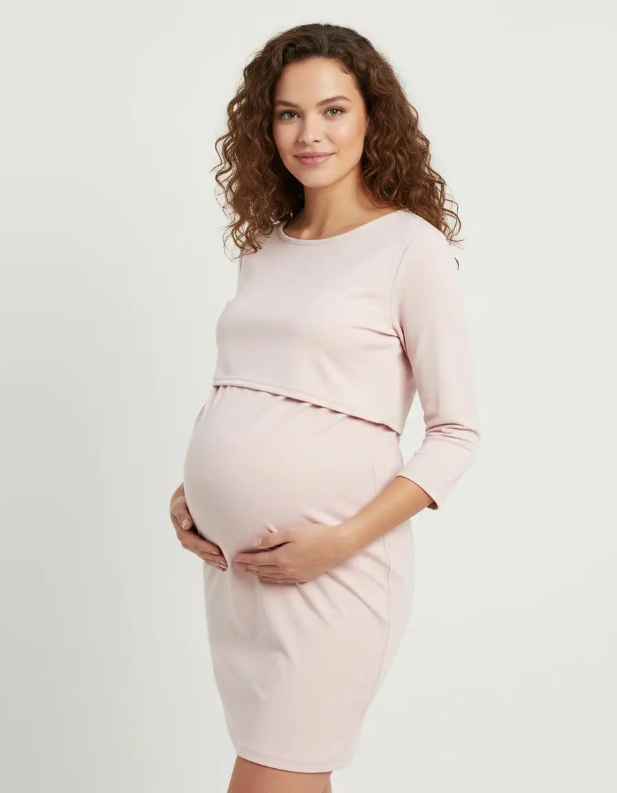 Woman in a light pink, round neck, 3/4 sleeve nursing top with feeding port, cradling her baby bump.