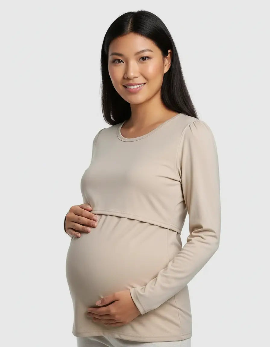 Smiling woman in a beige long-sleeve round neck nursing top with feeding port, cradling her baby bump.